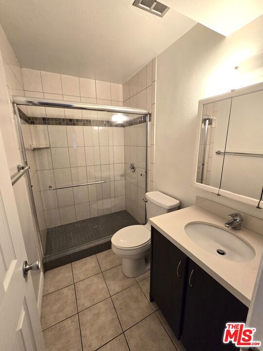 bathroom featuring tile patterned floors, walk in shower, vanity, and toilet