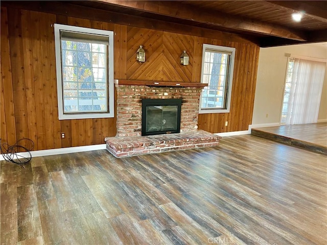 unfurnished living room with a fireplace, beam ceiling, dark wood-type flooring, and wood walls