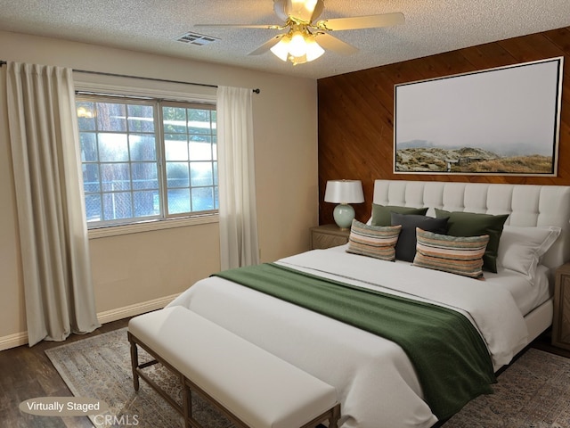 bedroom featuring ceiling fan, dark hardwood / wood-style flooring, a textured ceiling, and wooden walls