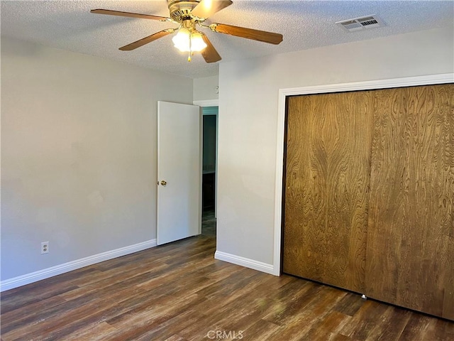 unfurnished bedroom with ceiling fan, a closet, dark wood-type flooring, and a textured ceiling