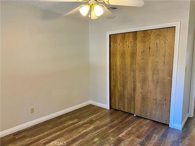 unfurnished bedroom featuring ceiling fan, a closet, dark wood-type flooring, and a textured ceiling