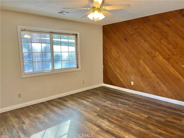 empty room with wooden walls, dark wood-type flooring, and a textured ceiling