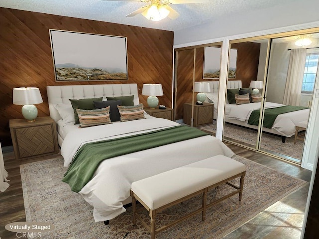 bedroom featuring ceiling fan, hardwood / wood-style floors, a textured ceiling, wooden walls, and two closets