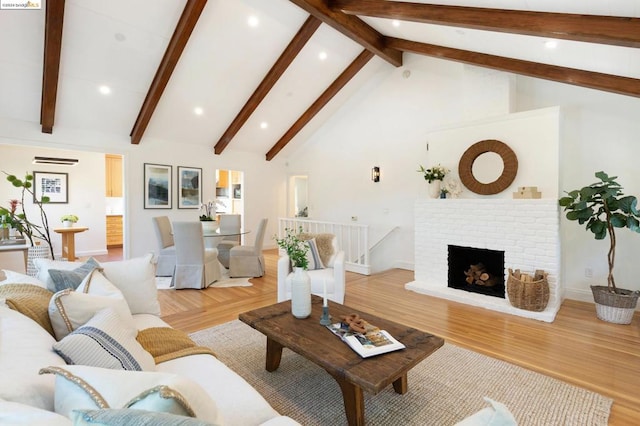 living room with light hardwood / wood-style floors, a brick fireplace, and vaulted ceiling with beams