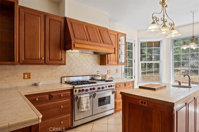 kitchen featuring custom exhaust hood, tasteful backsplash, hanging light fixtures, range with two ovens, and sink