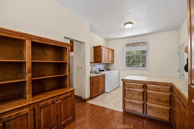 kitchen with sink, light wood-type flooring, a textured ceiling, washing machine and clothes dryer, and tile counters