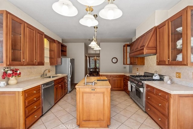 kitchen with appliances with stainless steel finishes, sink, decorative light fixtures, custom range hood, and a kitchen island with sink