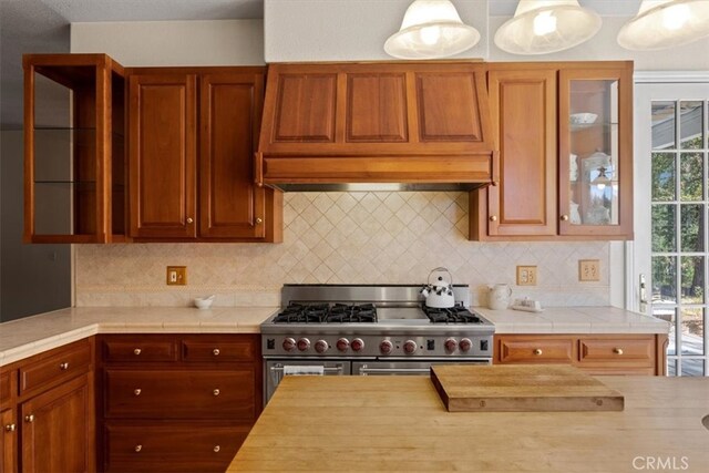 kitchen with custom range hood, stainless steel range, hanging light fixtures, and backsplash