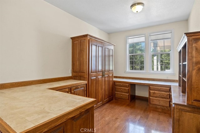 home office with a textured ceiling, built in desk, and wood-type flooring