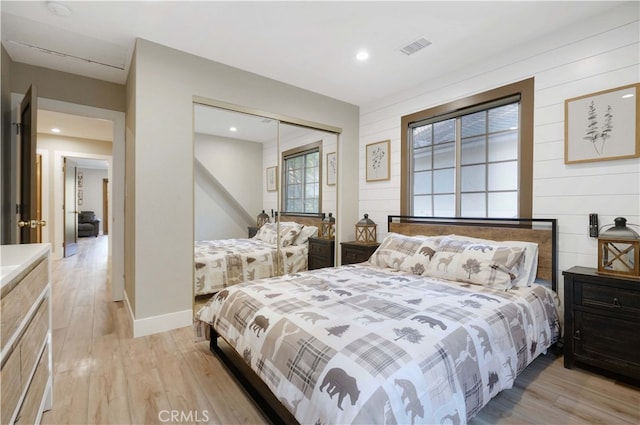 bedroom with light hardwood / wood-style flooring, wooden walls, and a closet