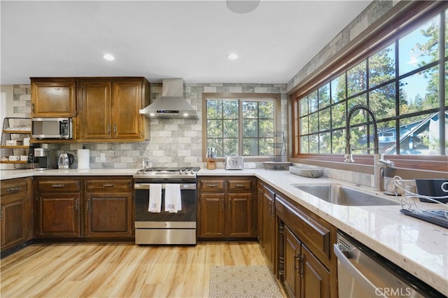 kitchen with sink, wall chimney exhaust hood, backsplash, stainless steel appliances, and light wood-type flooring