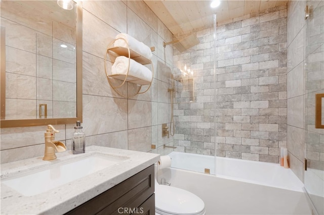 full bathroom with tiled shower / bath combo, toilet, vanity, and tile walls