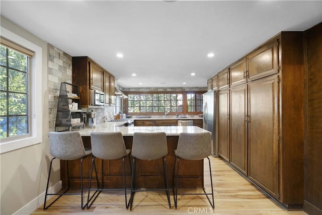 kitchen with appliances with stainless steel finishes, light hardwood / wood-style floors, kitchen peninsula, and a kitchen bar