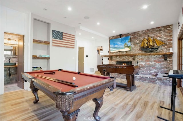 recreation room with pool table, brick wall, light wood-type flooring, and a brick fireplace