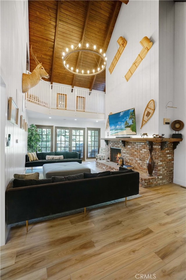 living room featuring a brick fireplace, a notable chandelier, light hardwood / wood-style floors, and high vaulted ceiling