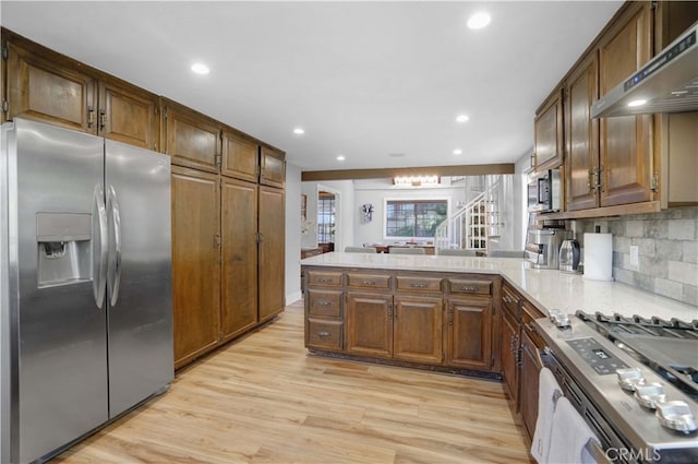 kitchen with kitchen peninsula, light hardwood / wood-style flooring, backsplash, wall chimney range hood, and appliances with stainless steel finishes