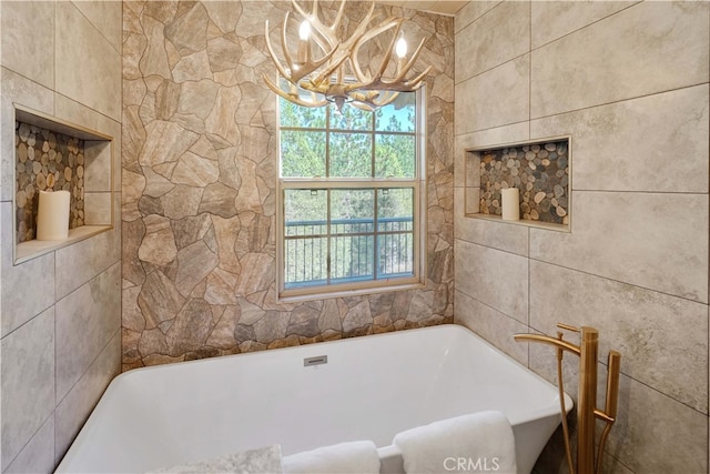 bathroom featuring tile walls, a tub, and a notable chandelier