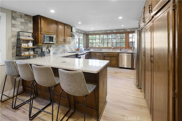 kitchen with light stone counters, a breakfast bar, kitchen peninsula, stainless steel appliances, and light hardwood / wood-style flooring