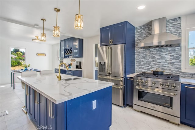 kitchen featuring sink, high end appliances, a center island with sink, wall chimney exhaust hood, and blue cabinetry