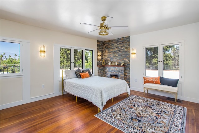 bedroom with french doors, a stone fireplace, dark hardwood / wood-style floors, and ceiling fan