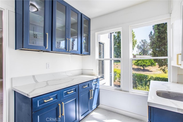 bar with blue cabinets, light stone countertops, and plenty of natural light