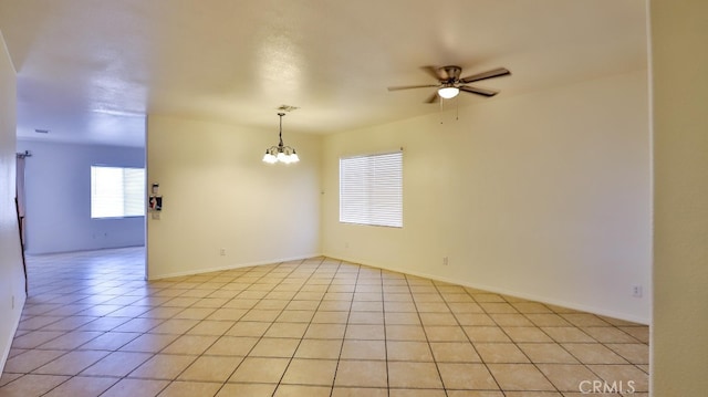 tiled empty room featuring ceiling fan with notable chandelier