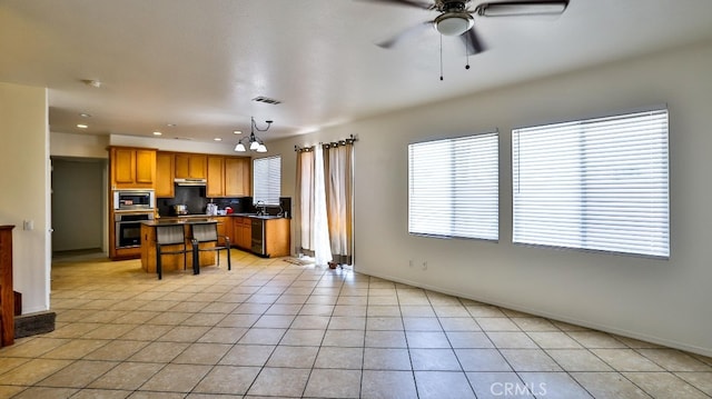 kitchen with light tile patterned flooring, decorative light fixtures, stainless steel appliances, a breakfast bar area, and ceiling fan with notable chandelier