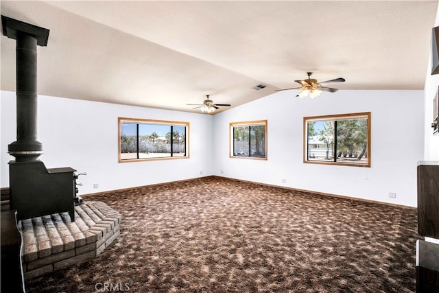 living room with a healthy amount of sunlight, carpet flooring, vaulted ceiling, and a wood stove