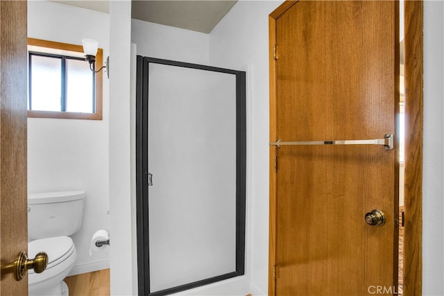 bathroom with wood-type flooring, a shower with shower door, and toilet