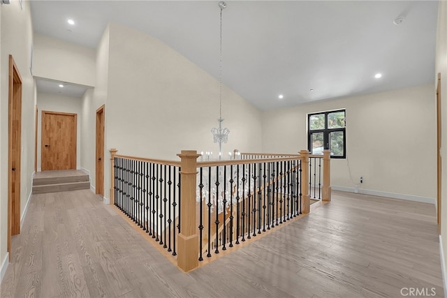 corridor featuring light wood-type flooring, an inviting chandelier, and high vaulted ceiling