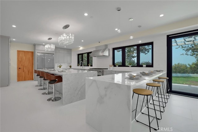 kitchen featuring pendant lighting, light stone counters, a breakfast bar area, and wall chimney range hood