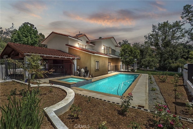 pool at dusk featuring an in ground hot tub