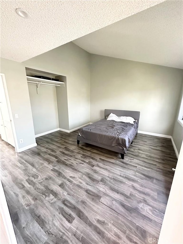 bedroom with a closet, vaulted ceiling, baseboards, and wood finished floors