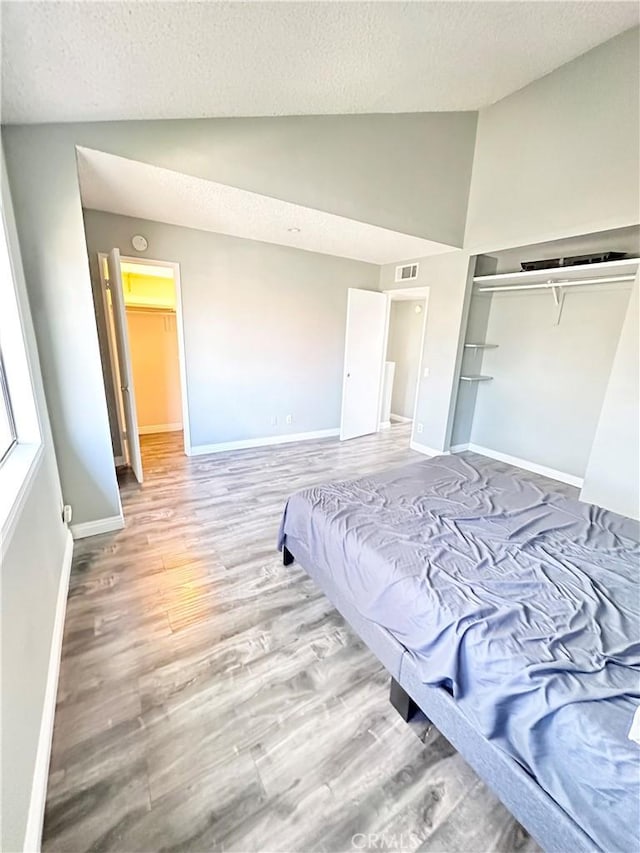 bedroom with vaulted ceiling, a textured ceiling, baseboards, and wood finished floors