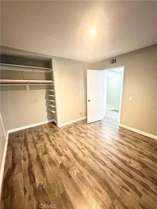 unfurnished bedroom with a closet, visible vents, baseboards, and wood finished floors