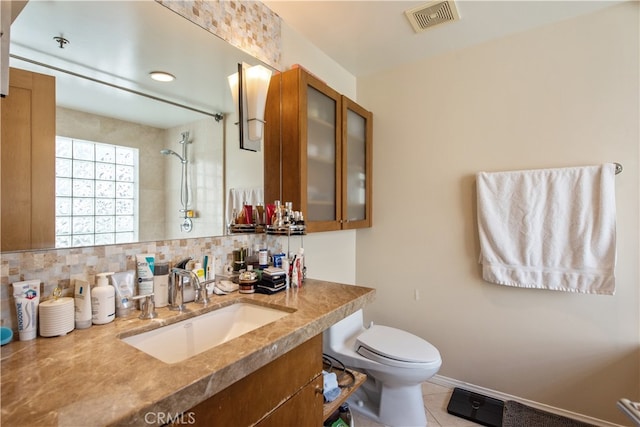 bathroom with vanity, backsplash, a tile shower, tile patterned floors, and toilet