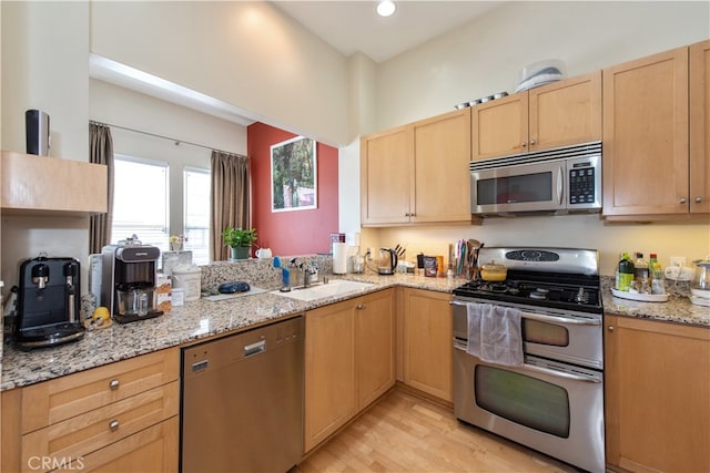 kitchen with light wood-type flooring, light stone countertops, stainless steel appliances, light brown cabinets, and sink