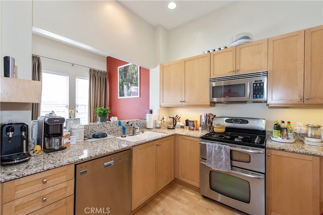 kitchen with light wood-type flooring, light stone countertops, sink, kitchen peninsula, and appliances with stainless steel finishes