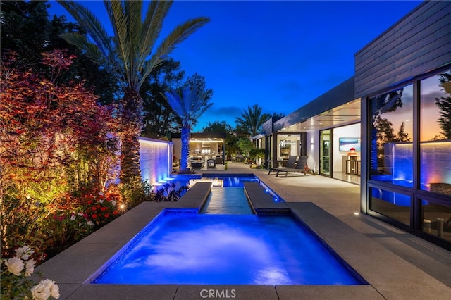 pool at dusk featuring a hot tub and a patio area