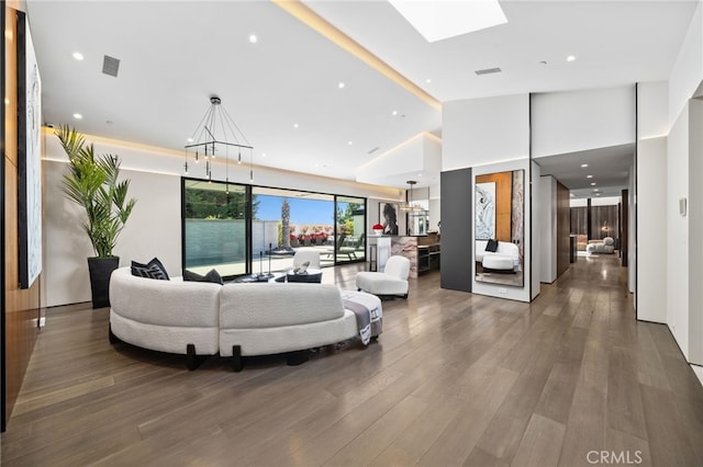 living room with dark hardwood / wood-style flooring, a skylight, high vaulted ceiling, and an inviting chandelier