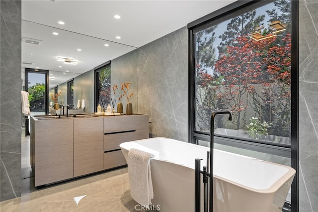 bathroom with a tub to relax in, vanity, expansive windows, and tile walls