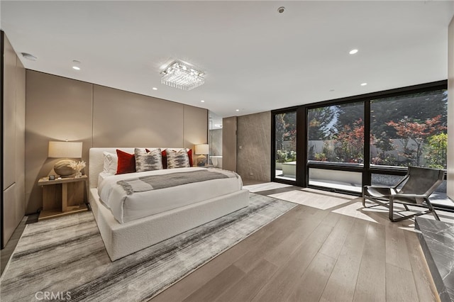 bedroom with floor to ceiling windows, light hardwood / wood-style floors, and access to exterior