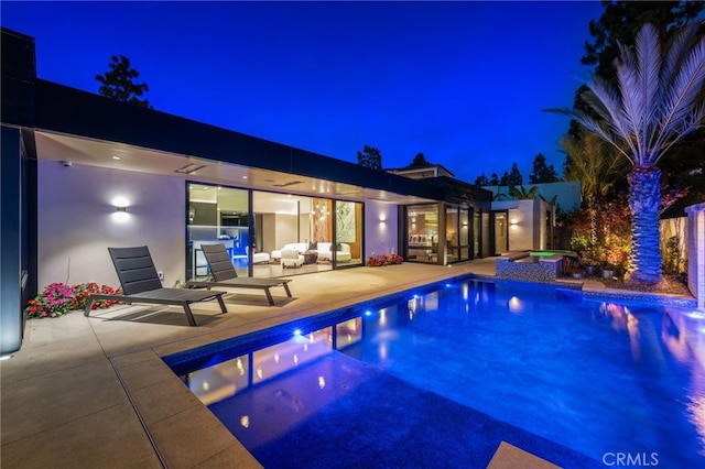 pool at twilight featuring an in ground hot tub, an outdoor hangout area, and a patio area