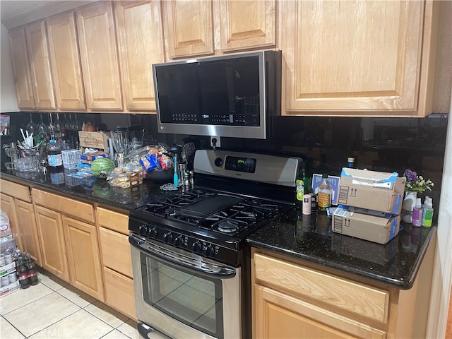 kitchen with light brown cabinetry, backsplash, stainless steel appliances, dark stone counters, and light tile patterned floors