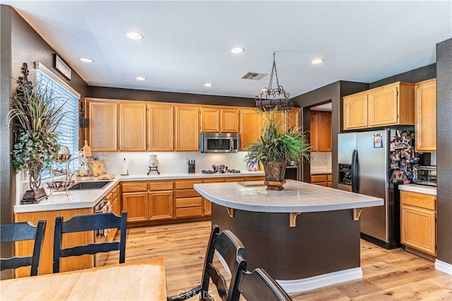 kitchen with appliances with stainless steel finishes, light wood-type flooring, decorative light fixtures, and sink