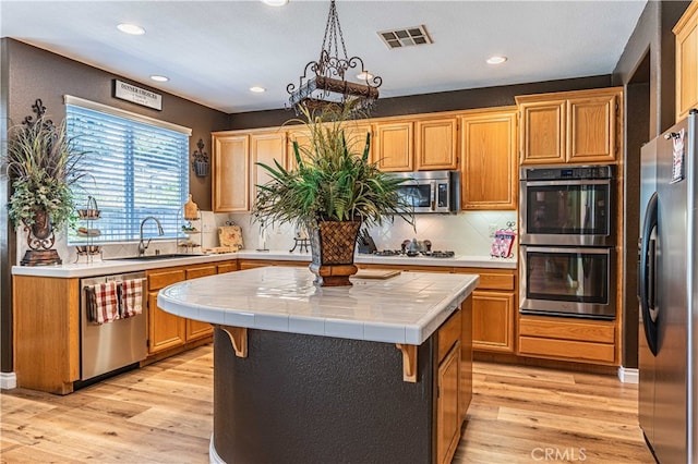 kitchen featuring sink, a kitchen island, light hardwood / wood-style flooring, stainless steel appliances, and tile counters