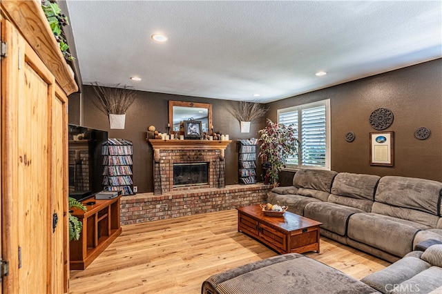 living room with a brick fireplace, a textured ceiling, and light hardwood / wood-style flooring