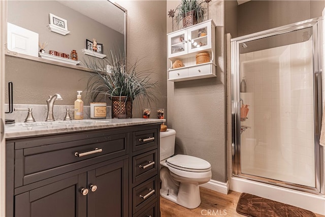 bathroom featuring wood-type flooring, toilet, vanity, and a shower with shower door