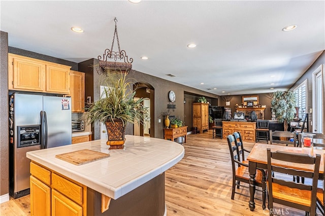 kitchen with stainless steel fridge, tile countertops, a center island, light brown cabinetry, and light wood-type flooring