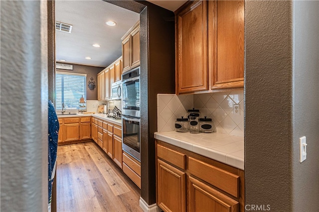 kitchen featuring sink, backsplash, tile countertops, stainless steel appliances, and light wood-type flooring